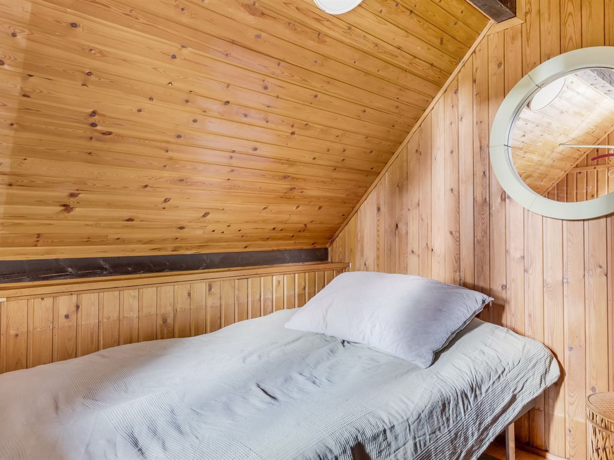 Interior em madeira com cama, um espelho redondo e teto inclinado.