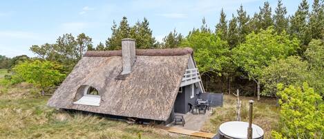 Een rieten huis met schoorsteen, een klein terras met tuinmeubels en een hottub in een natuurlijke omgeving.