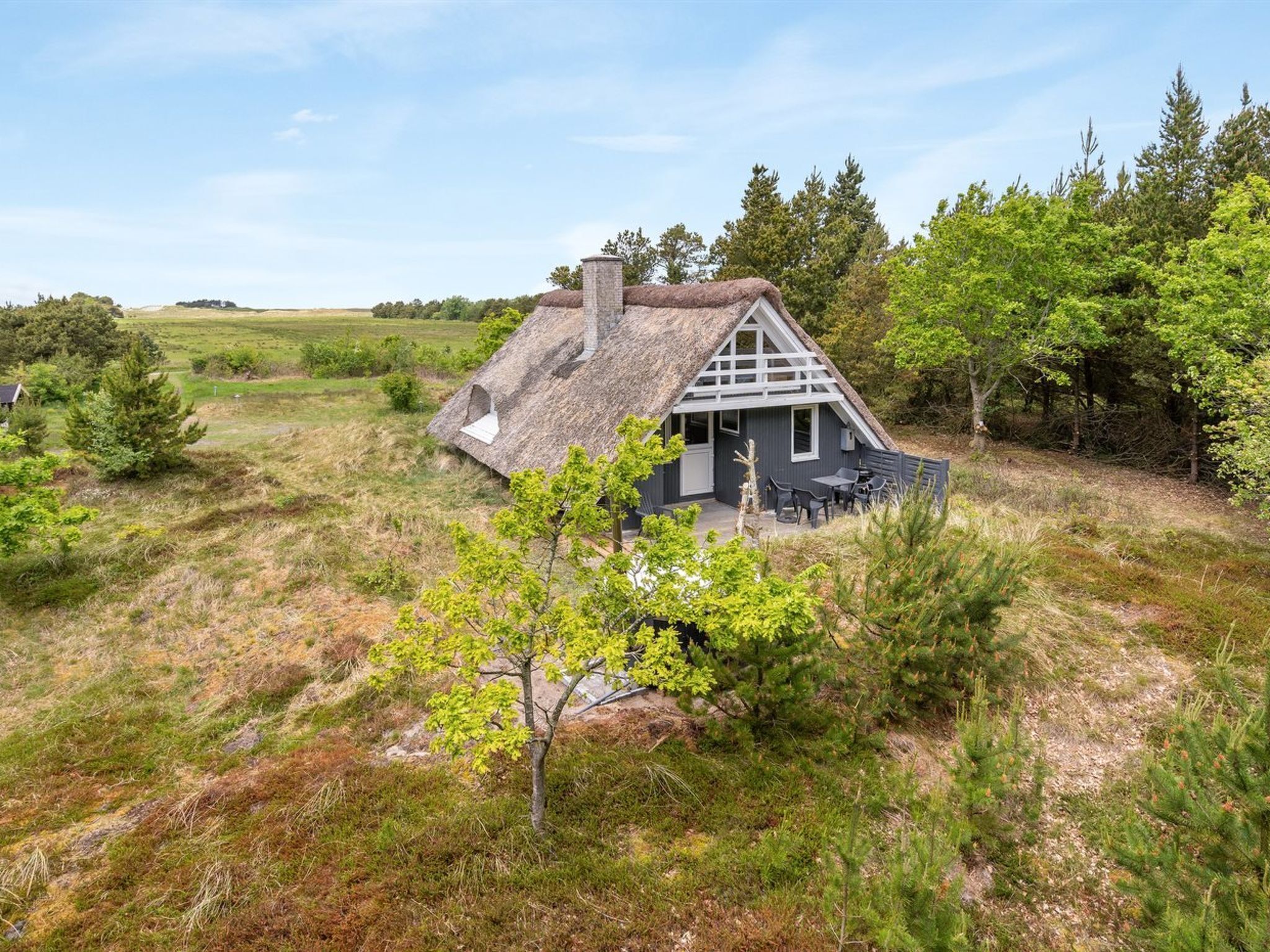 Ein Haus mit Strohdach und geneigtem Dach, umgeben von Bäumen und Gras.