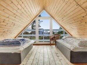 Une chambre mansardée triangulaire avec deux lits, une chaise en osier et une vue à travers une porte vitrée.