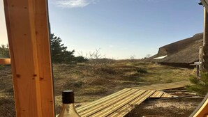 A wooden bench with two wine glasses and a bottle, overlooking a grassy landscape with a thatched-roof structure. - "Antero" - 4km from the sea by Interhome (Rømø)