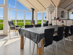 Un espace repas comprenant une table, des chaises, une cheminée et de grandes fenêtres donnant sur un paysage verdoyant.