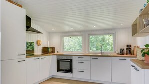 Una cocina moderna con armarios blancos, horno integrado y ventana con vistas a zonas verdes.