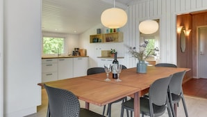 Una cocina moderna con armarios blancos, una mesa de comedor de madera y dos lámparas colgantes.