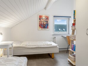 Ein Schlafzimmer mit Bett, Fenster, Heizkörper, Bücherregal und einem Bild an der Wand.