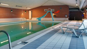Una piscina interna con uno scivolo blu, pavimento piastrellato e poltroncine relax.