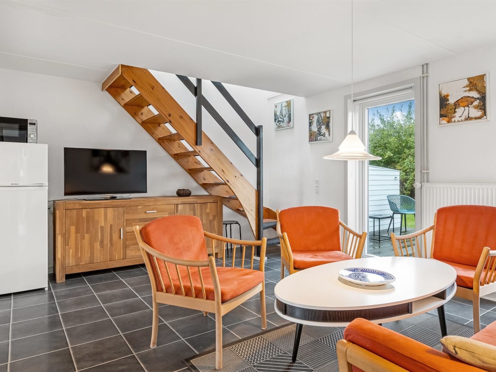 Ein modernes Wohnzimmer mit einer Holztreppe, einem Fernseher, einem Esstisch und orangefarbenen Stühlen.