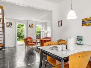 Ein Essbereich mit Tisch für vier Personen, Stühlen, einer weißen Deckenleuchte und Blick auf Grünfläche draußen.