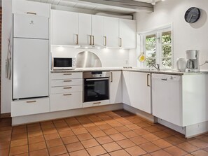 Uma cozinha moderna com armários brancos, forno embutido, micro-ondas e cafeteira.