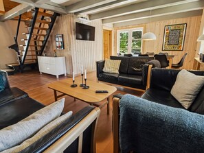 Uma sala de estar acolhedora com escadas, uma TV de tela plana, uma área de jantar e uma janela com vista.
