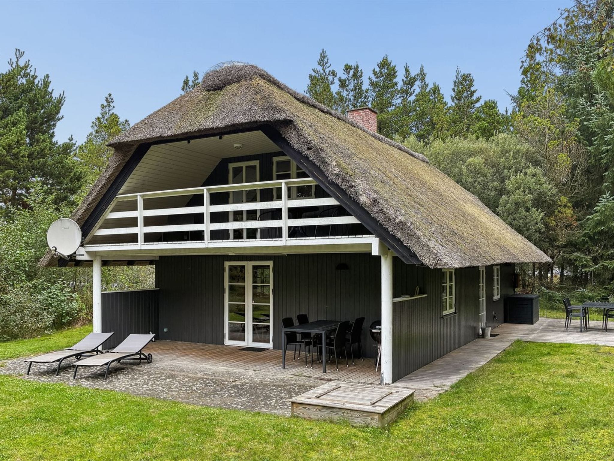 A two-story house with a thatched roof, a balcony, and a patio area with outdoor furniture.