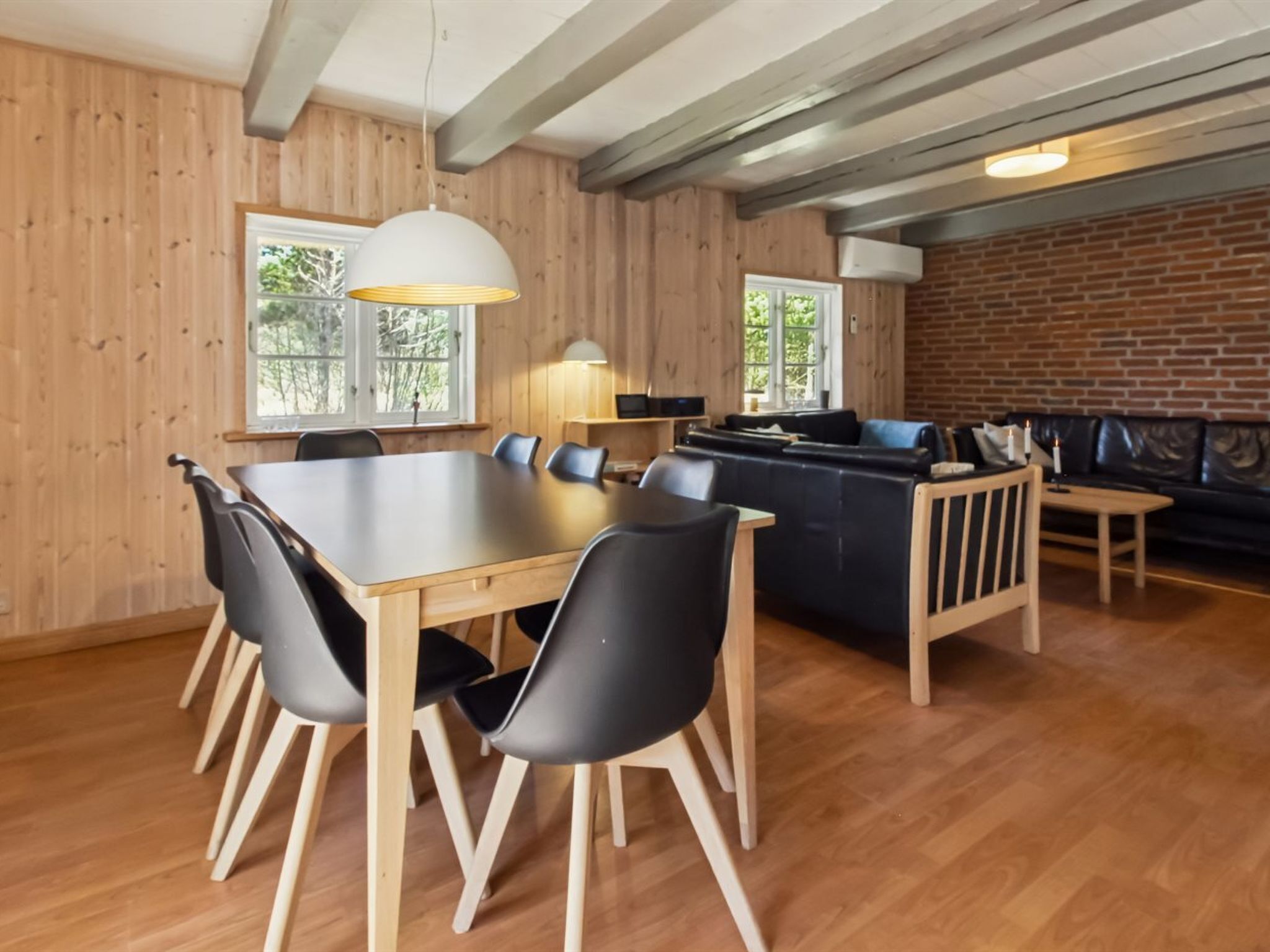 A dining area with a wooden table and chairs, a black sofa, and a brick wall.