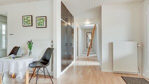 A modern, well-lit room with a wooden floor, a dining table with a checkered tablecloth, a black chair, and a vase with flowers. There are two framed artworks on the wall, a radiator, and a door leading to another room. - "Toralf" - 3.5km from the sea by Interhome (Rømø)