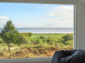 A room with a large window overlooking a coastal landscape with a tree and grassy fields.