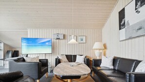 Ett modernt vardagsrum med en stor TV med platt skärm, lädersoffor, ett runt soffbord och ett träpanelat tak.