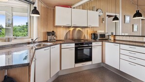 Ett modernt kök med vita skåp, en rostfri köksfläkt, en inbyggd ugn och ett stort fönster som släpper in naturligt ljus.