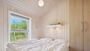 Ett sovrum med en säng, ett fönster, träväggar och en hylla med böcker.