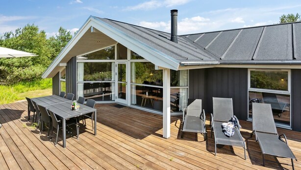 Ett modernt hus med en stor terrass, utomhusmöbler och en skorsten.