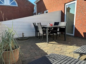 En terrasse med et bord, stole, en potteplante og en murstensvæg.
