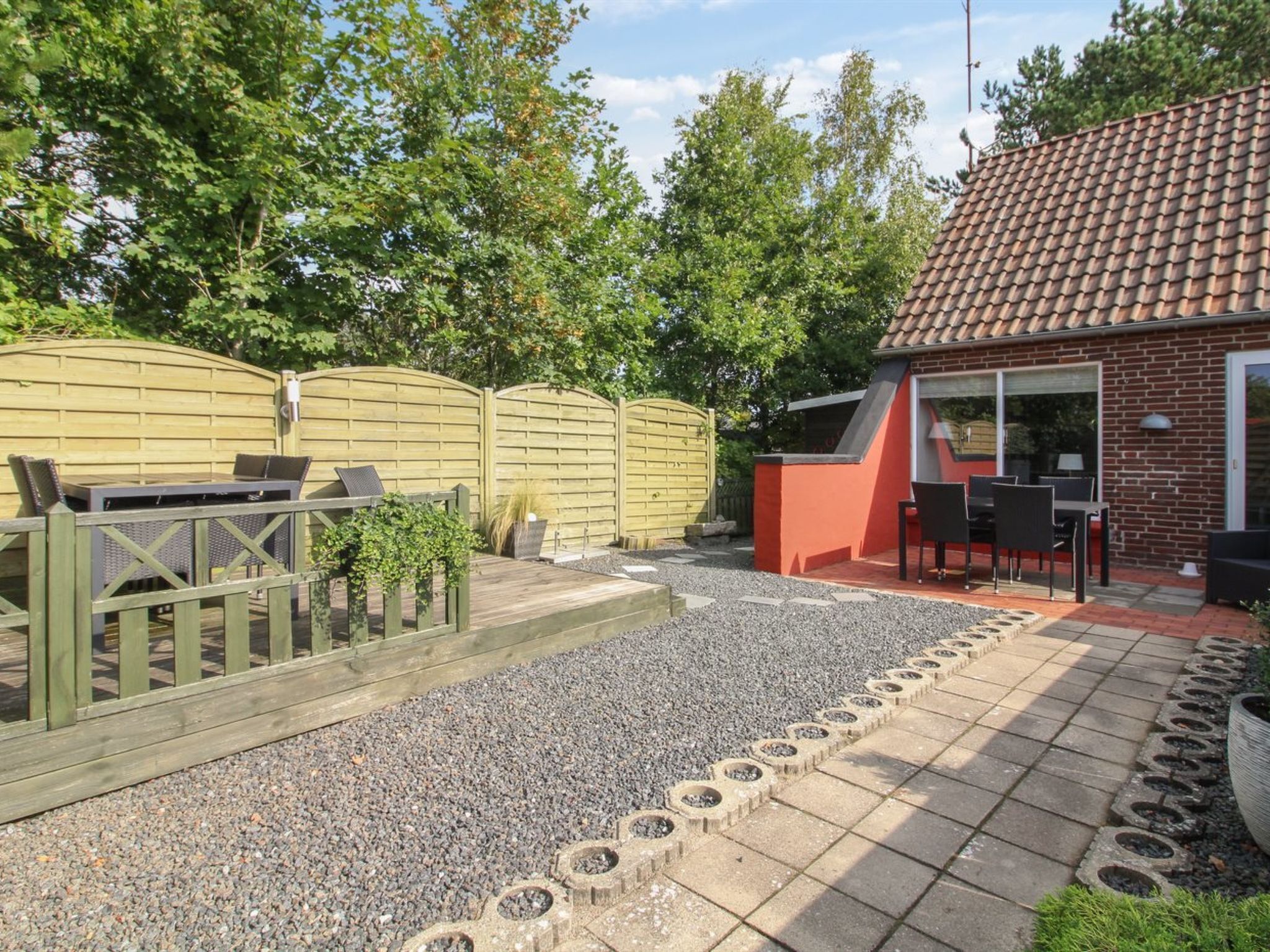 Een terras met een barbecue, buitenzitplaatsen en een houten omheining.