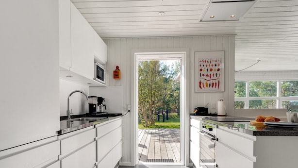 A modern kitchen with white cabinetry, a black countertop, and a view of the outdoors through a glass door. - "Tora" - 3km from the sea by Interhome (Rømø)
