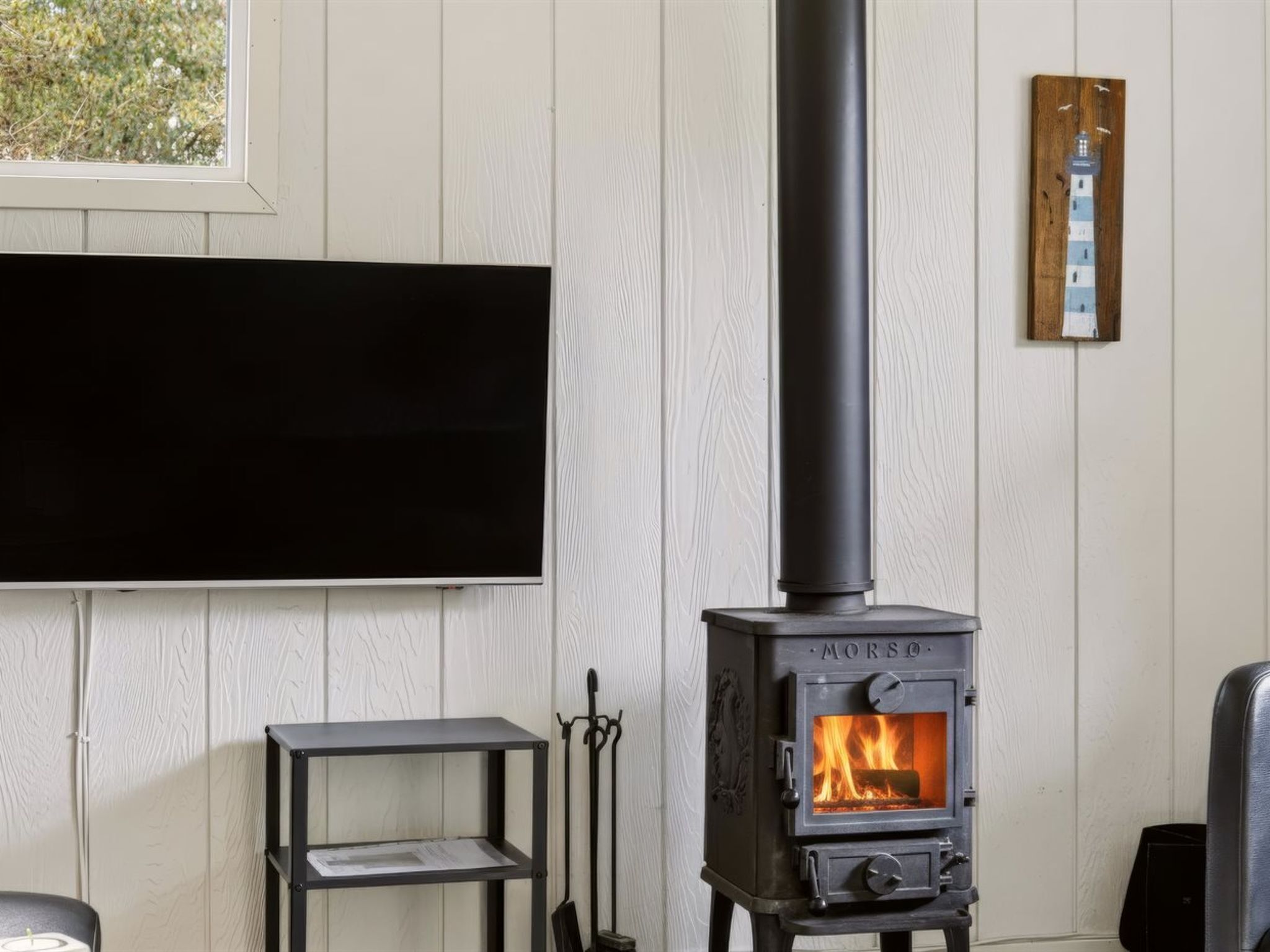 A room with a wood-burning stove, a mounted television, and a small shelf unit.