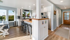 A modern kitchen with white cabinets, a central island, and a dining area with bar stools. - The Cachalot MCA# 50330- Oceanview, 1/4 block to beach, Dogs OK, Game room (Manzanita)
