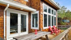 A wooden house with large glass doors, a wooden deck, and red chairs. - The Cachalot MCA# 50330- Oceanview, 1/4 block to beach, Dogs OK, Game room (Manzanita)