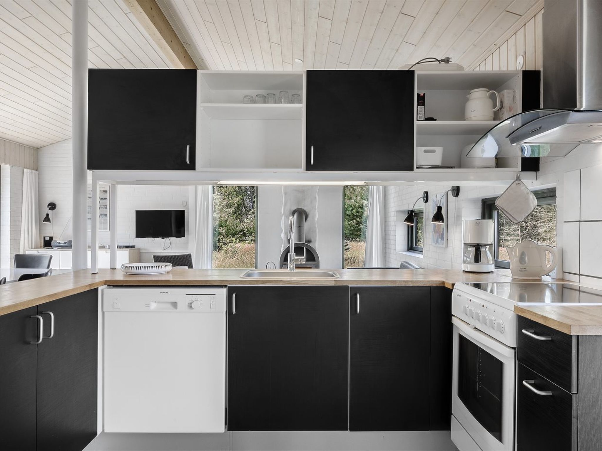 A modern kitchen with black and white cabinetry, a dishwasher, a stove, and a coffee maker.