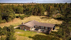 Una casa de un piso con techo inclinado, rodeada por un bosque frondoso.