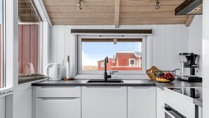 Eine moderne Küche mit weißen Schränken, einer schwarzen Spüle, einem Fenster mit Blick auf ein rotes Gebäude und einer Kaffeemaschine.