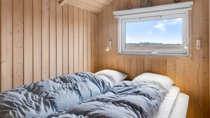 Ein Schlafzimmer mit Holzboden und -wänden, einem Fenster mit Blick auf ein Feld und einem Bett mit blauer Decke.