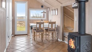 Ein gemütliches Zimmer mit Holzvertäfelung, einem Essbereich mit Tisch und Stühlen, einem großen Fenster und einem schwarzen Kaminofen.