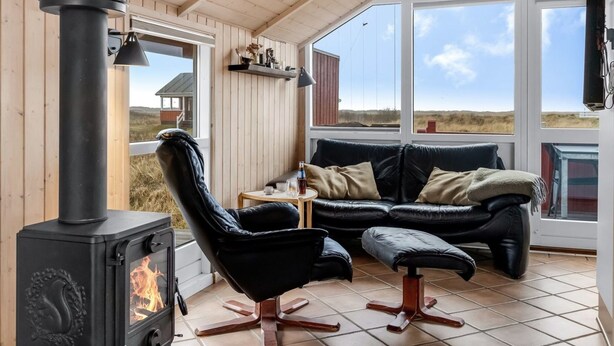 Ein gemütlicher Raum mit einer schwarzen Ledersofa, einem schwarzen Sessel und einem schwarzen Kaminofen.