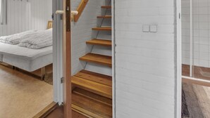 Une salle de bain moderne avec un escalier en bois, un espace douche et un lit recouvert d’une couverture blanche.