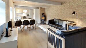 Una sala moderna con un sofá, un comedor con sillas, una chimenea y una cocina al fondo.