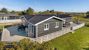 A modern wooden house with a deck, large windows, and a clear view of the surrounding landscape.