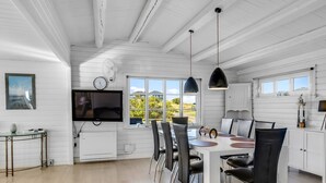 A modern kitchen with white cabinetry, a dining area with a round table and chairs, and a large window offering a view of greenery.
