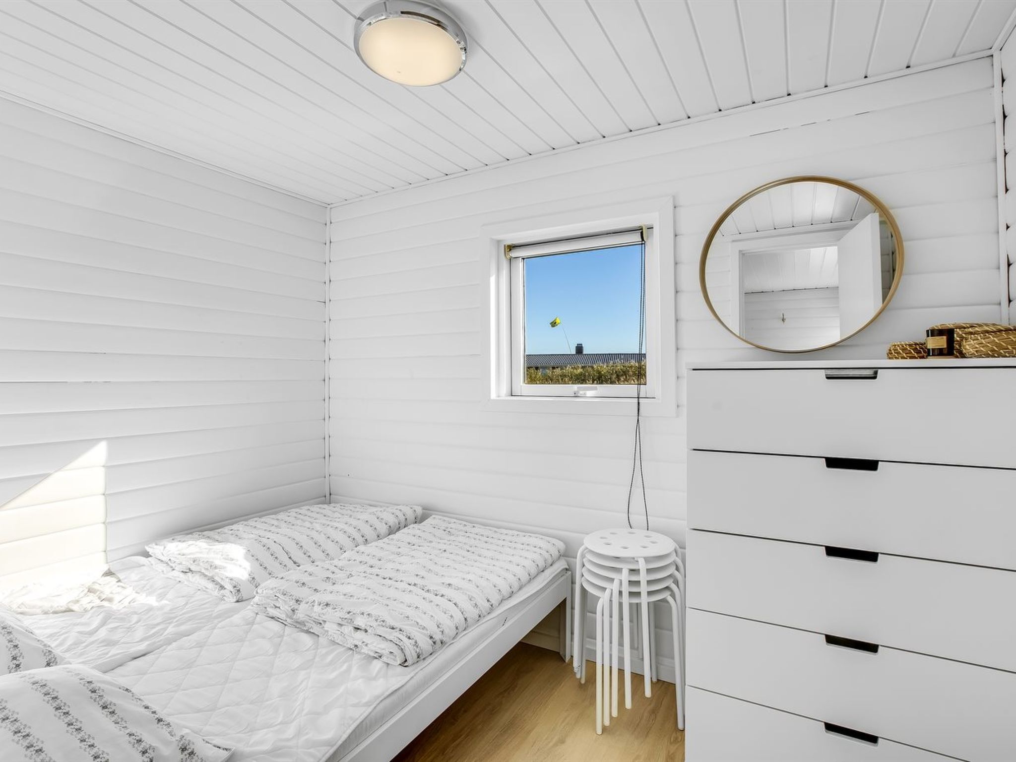 Une chambre à coucher minimaliste, avec un lit, une commode, un miroir et une fenêtre donnant sur un paysage verdoyant.