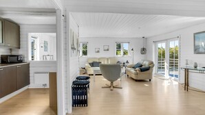 A spacious living area with a sofa, armchairs, and a dining table. There is a kitchen area with cabinets and a microwave.