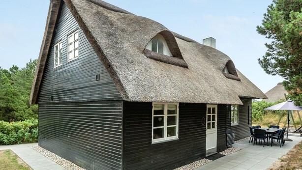 A black wooden house with a thatched roof and a small patio area with a table and chairs. - "Risto" - 2.3km from the sea by Interhome (Rømø)