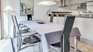 Uma cozinha moderna com armários brancos, eletrodomésticos de aço inoxidável e um espaço de refeições com mesa e cadeiras.