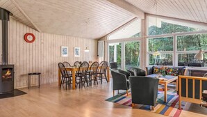 Een ruime kamer met houten plafond, een zithoek met tafel en stoelen, een bank en een open haard.