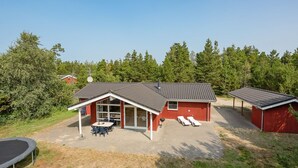 Een rode woning met een overdekte patio, een barbecueplaats en twee lounge fauteuils.
