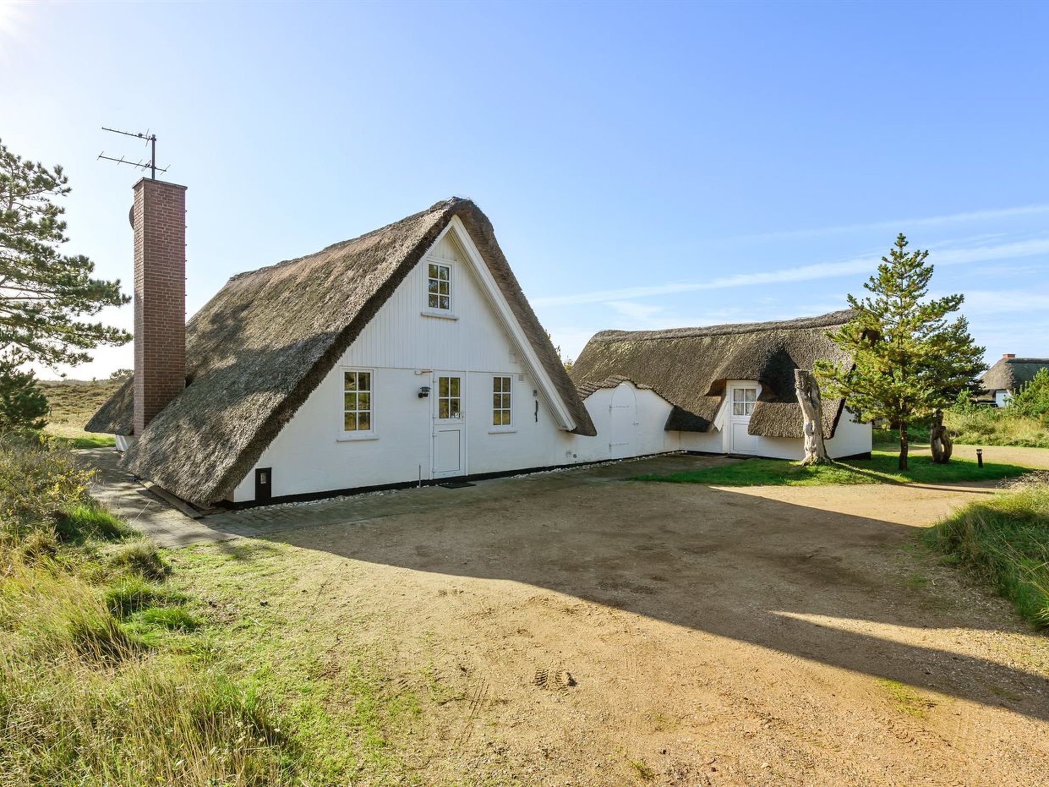 A traditional white building with a steeply pitched thatched roof, a brick chimney, and a small door.