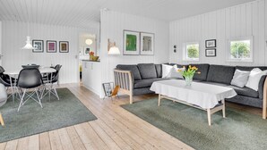 Een moderne woonkamer met een grijze bank, een eettafel met stoelen en een keuken op de achtergrond.