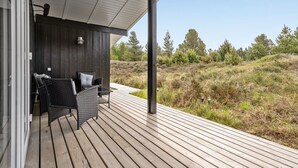 Een houten terras met twee rieten stoelen en een tafel, met uitzicht op een grasland met bomen.