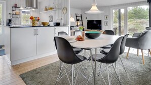 Een moderne keuken met witte kasten, een centraal eiland en een eethoek met zwarte stoelen en een ronde tafel.