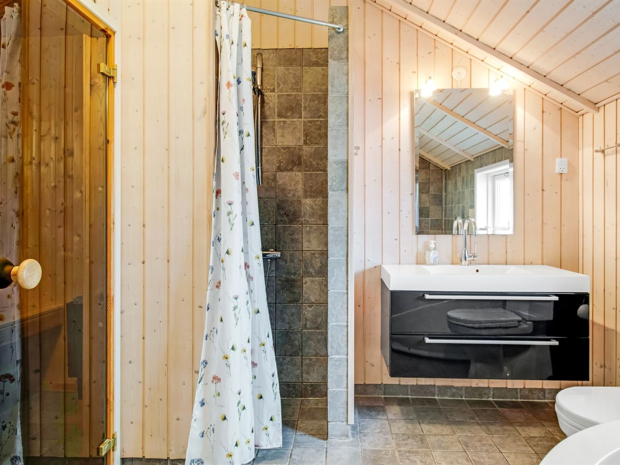 Een badkamer met houten wanden, douchegordijn, wastafel en toilet.