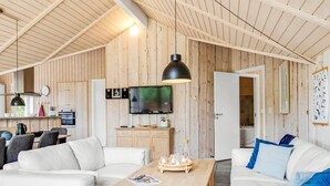 Een ruime woonkamer met een houten plafond, een televisie en een keuken in de achtergrond.